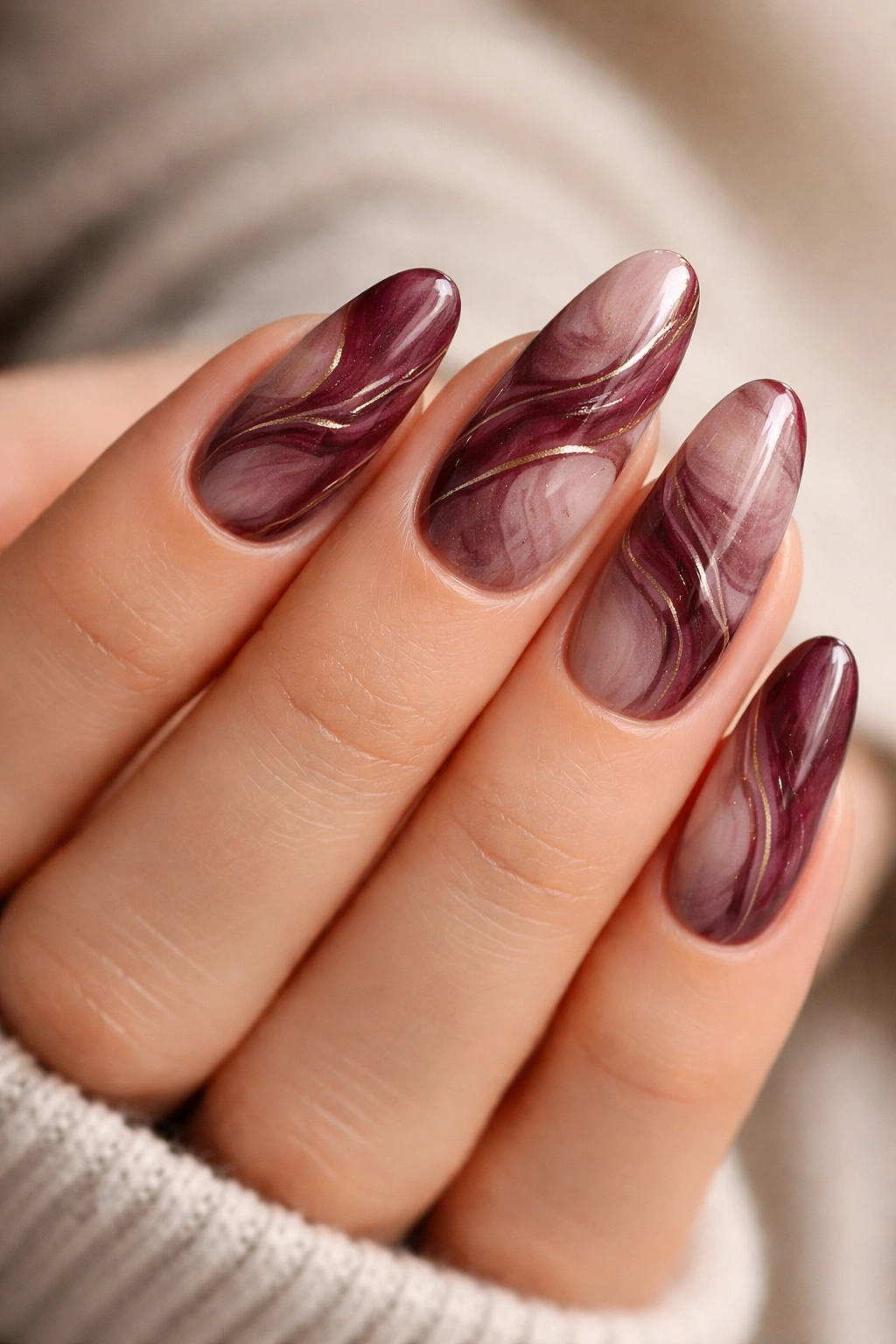 Close-up of burgundy marble swirls on long oval nails with taupe and gold veining