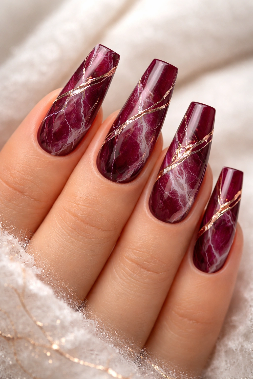 Close-up of burgundy coffin nails with white marble veining and rose gold accents