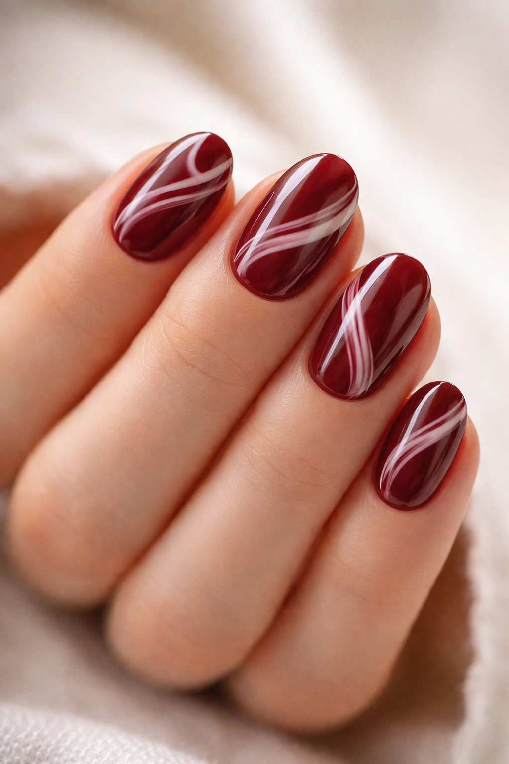 Close-up burgundy and milky white swirl nails on short oval nails.