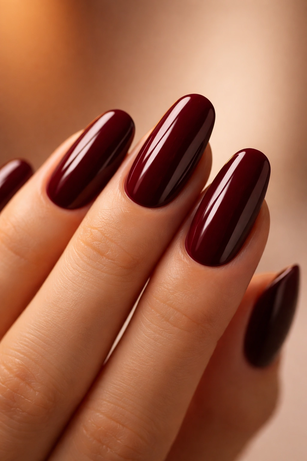 Close-up of glossy deep burgundy nails on a warm neutral background