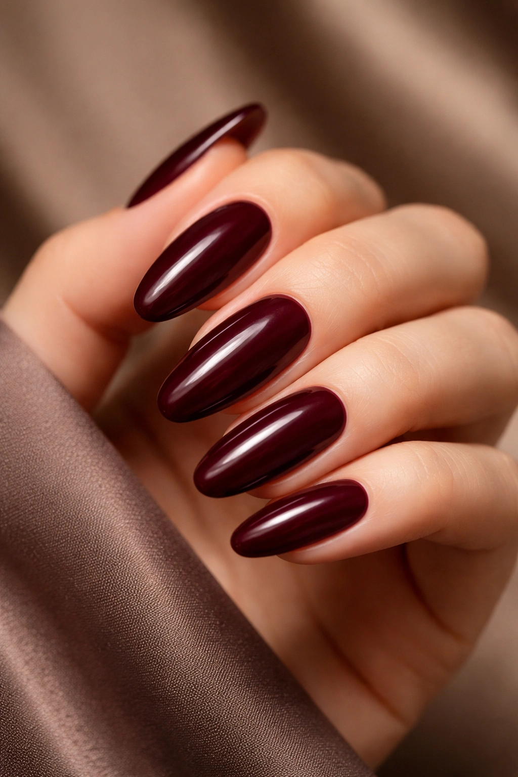 Close-up of long oval burgundy nails with glossy deep wine shade.