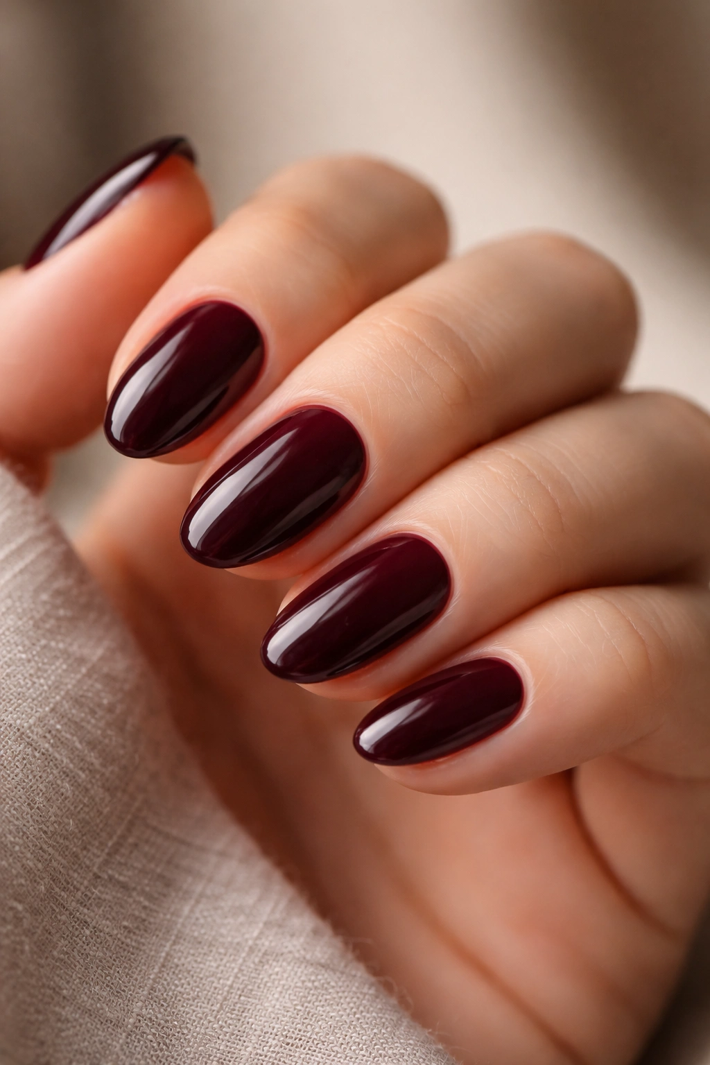 Close-up of short almond nails in deep burgundy polish