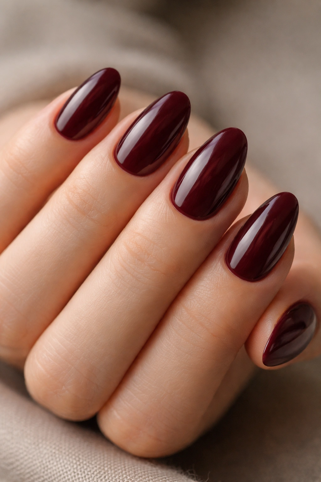 Close-up of burgundy short almond nails on hand.