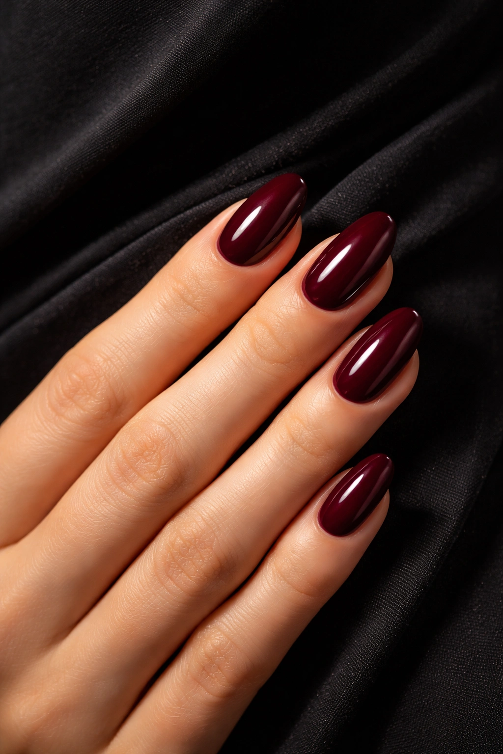 Close-up of burgundy nails with a glossy finish against black dress fabric
