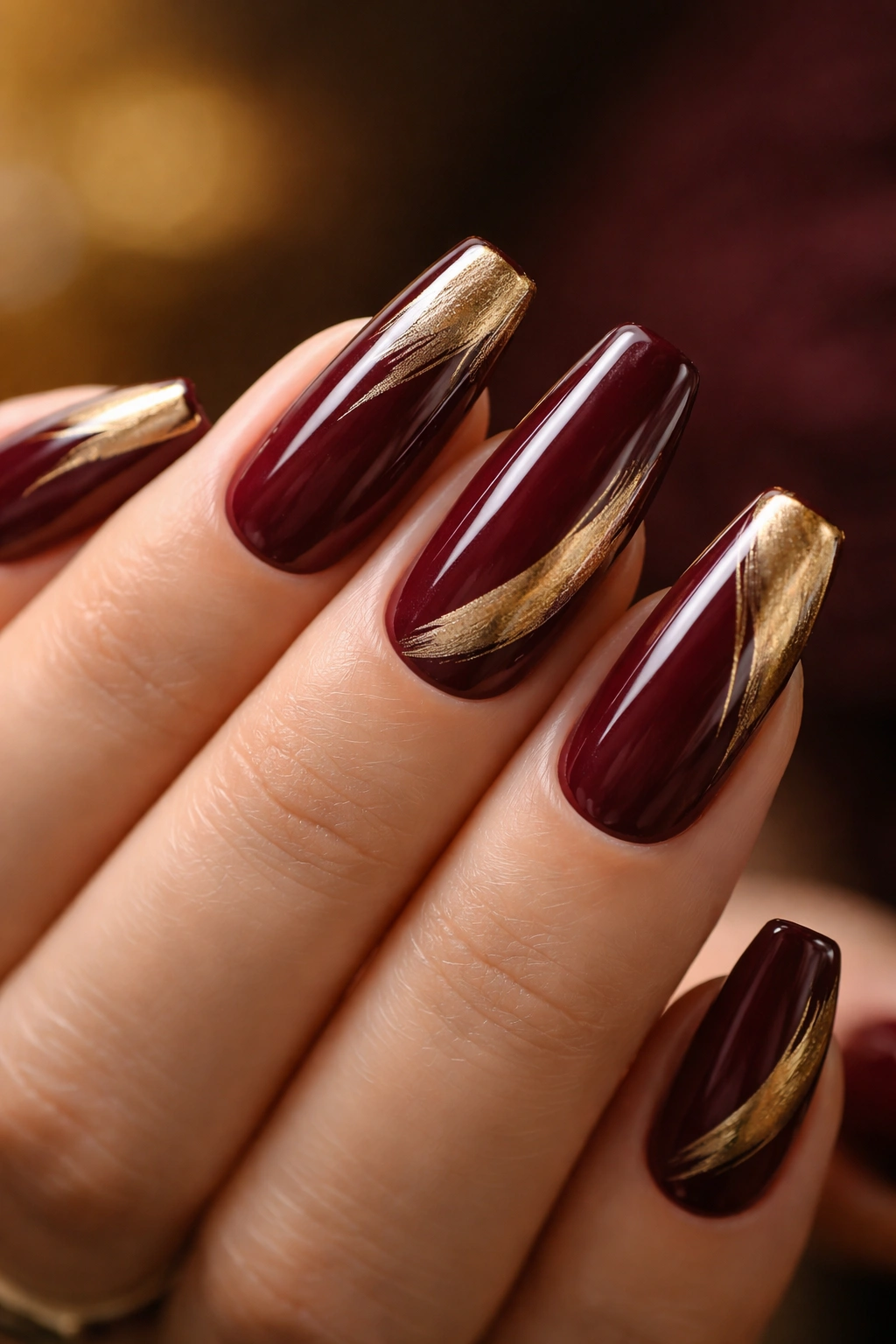 Close-up of deep burgundy ballerina nails with brushed gold accents