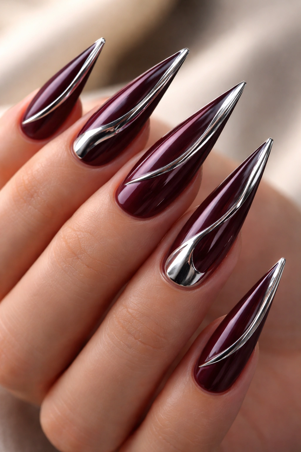 Burgundy stiletto nails with chrome accents and metallic stripes.