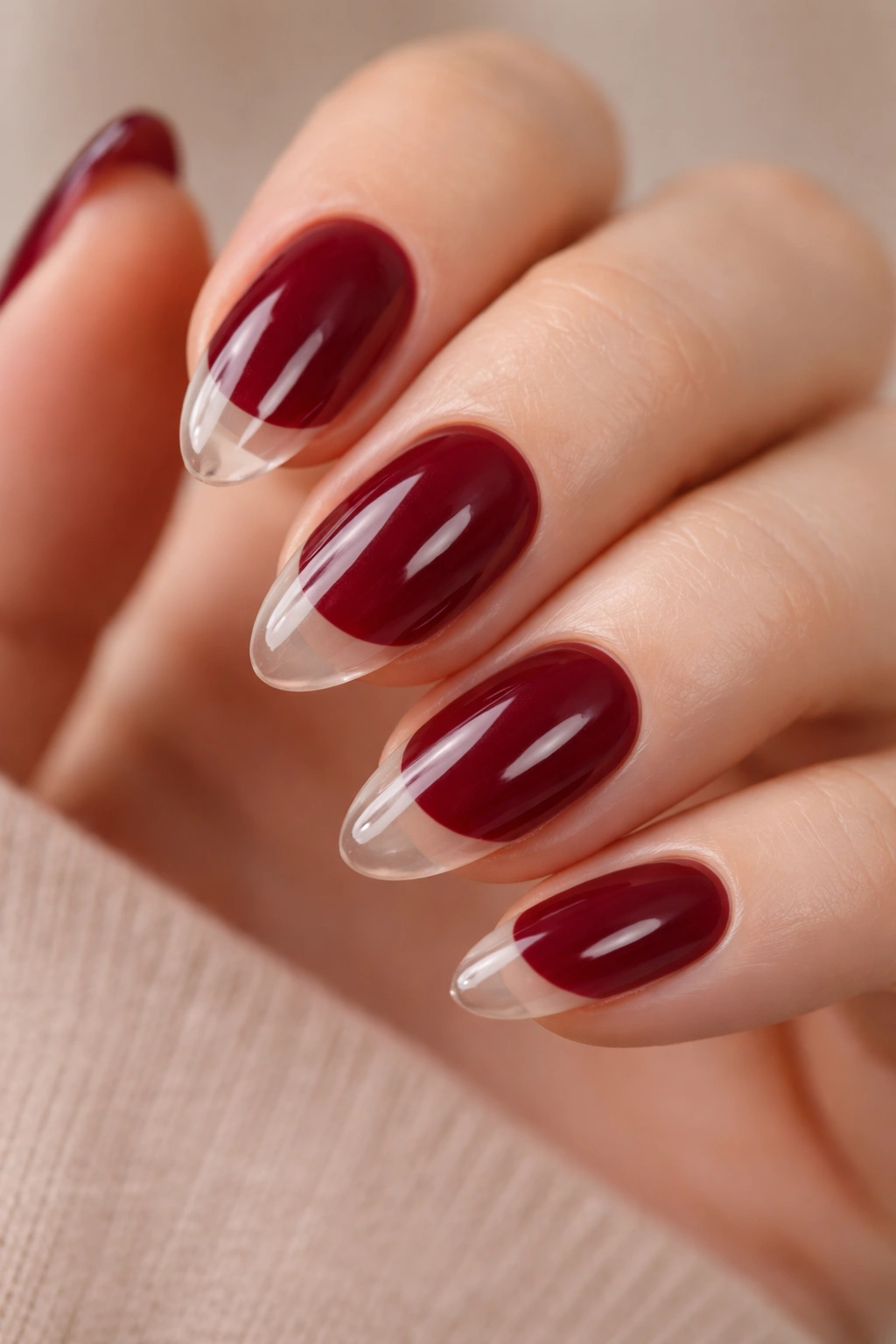 Close-up of short burgundy almond nails with clear tips and a crisp boundary