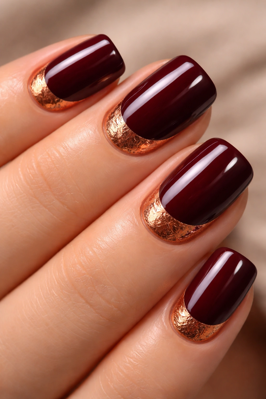 Close-up of deep burgundy nails with copper foil at the base