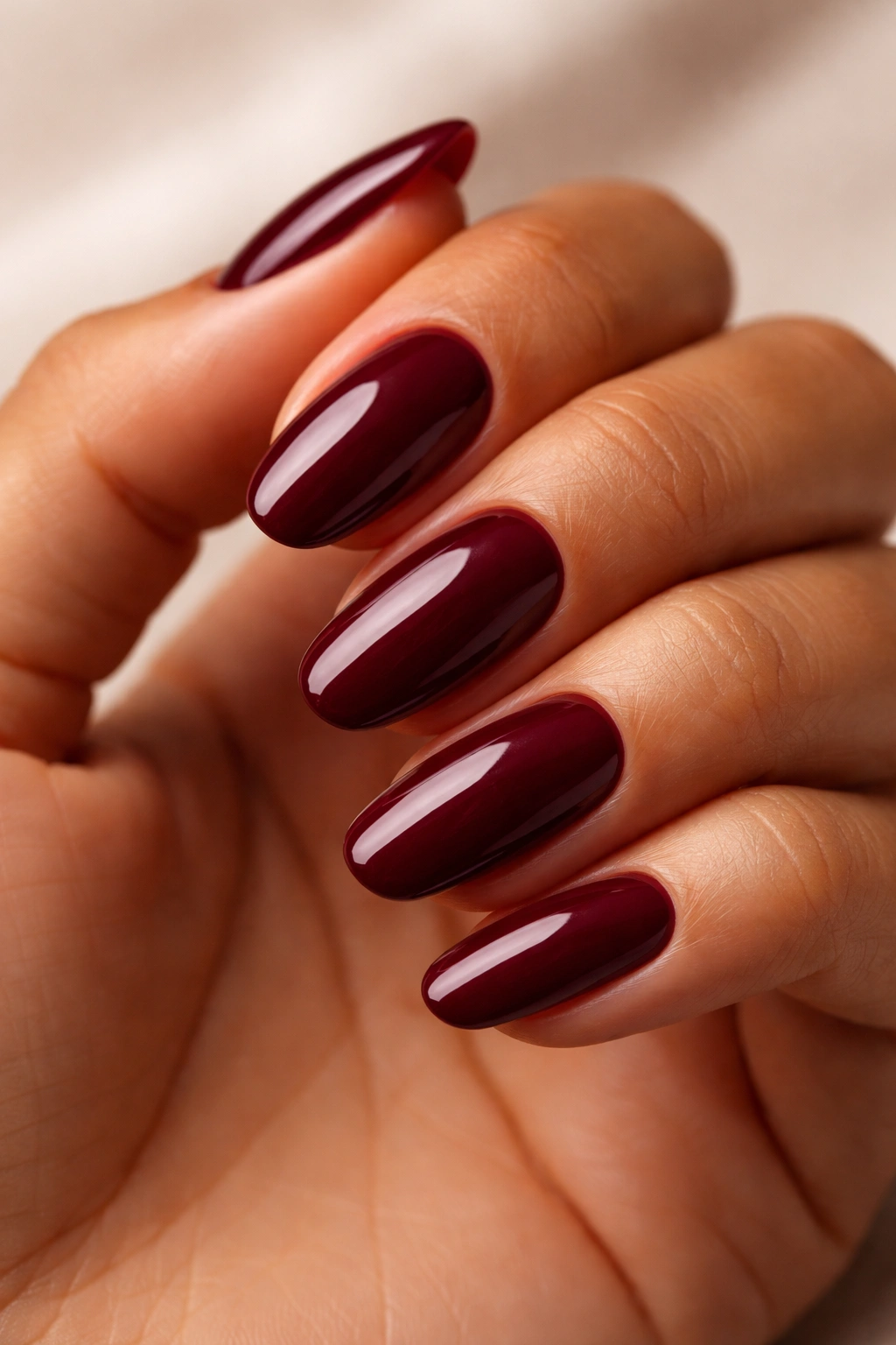 Close-up of hand with rich burgundy nails against a soft studio backdrop