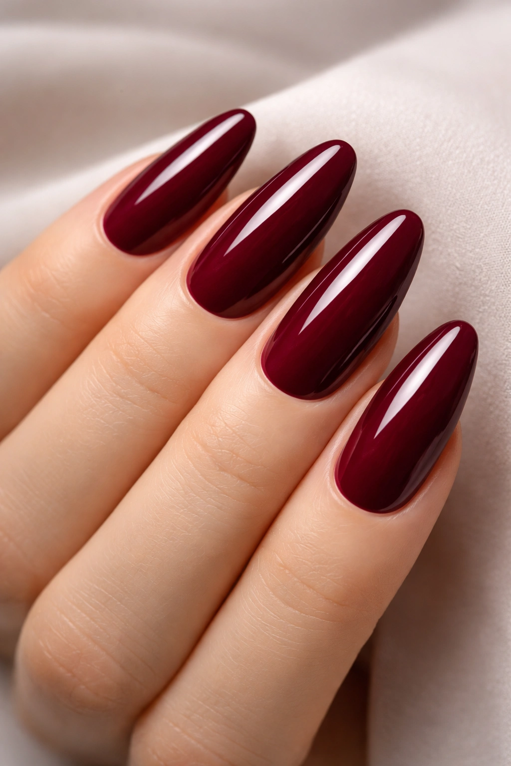 Close-up of long oval nails in deep burgundy with glossy finish