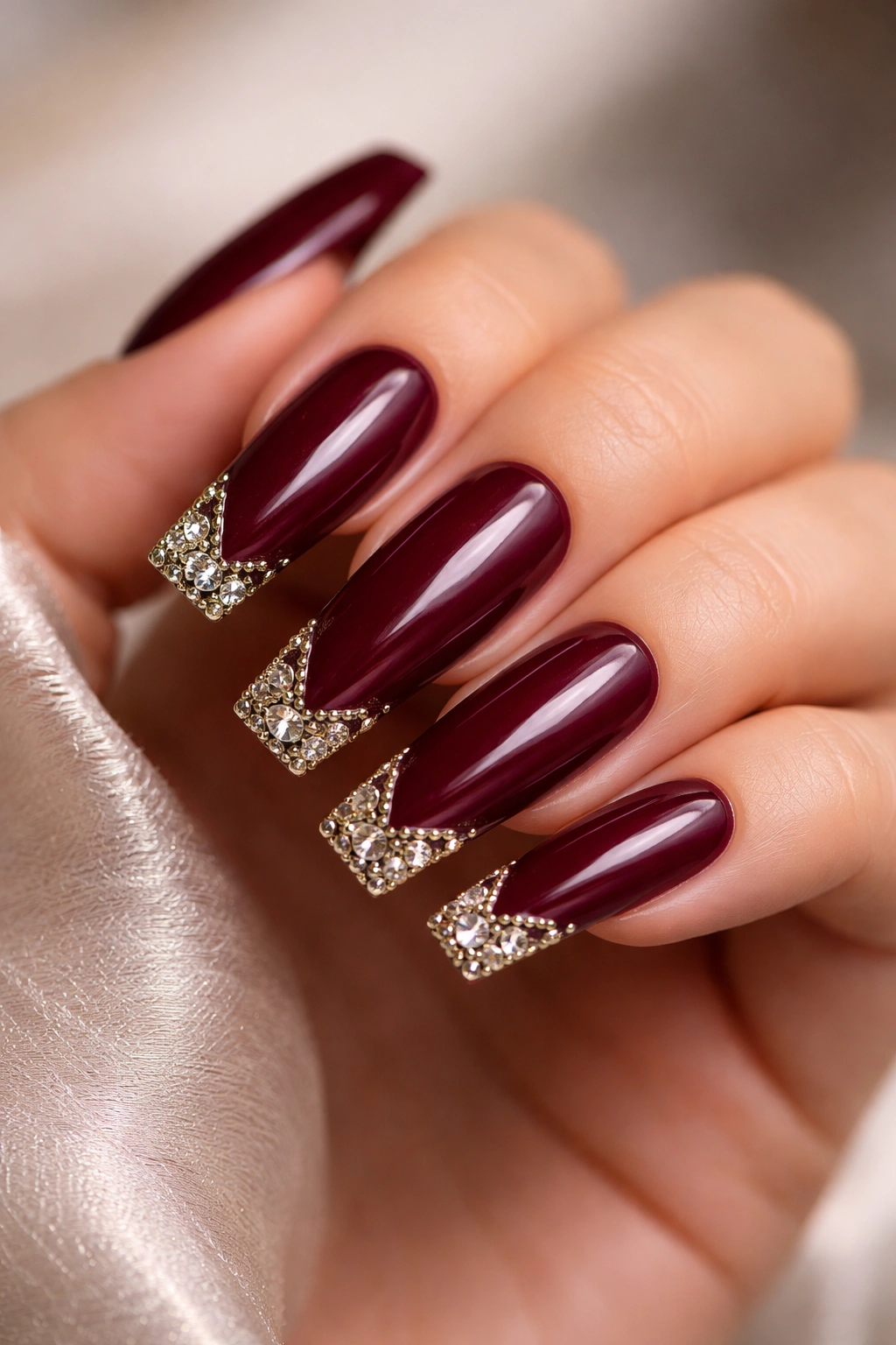 Close-up of burgundy coffin nails with corner rhinestones and metallic accents
