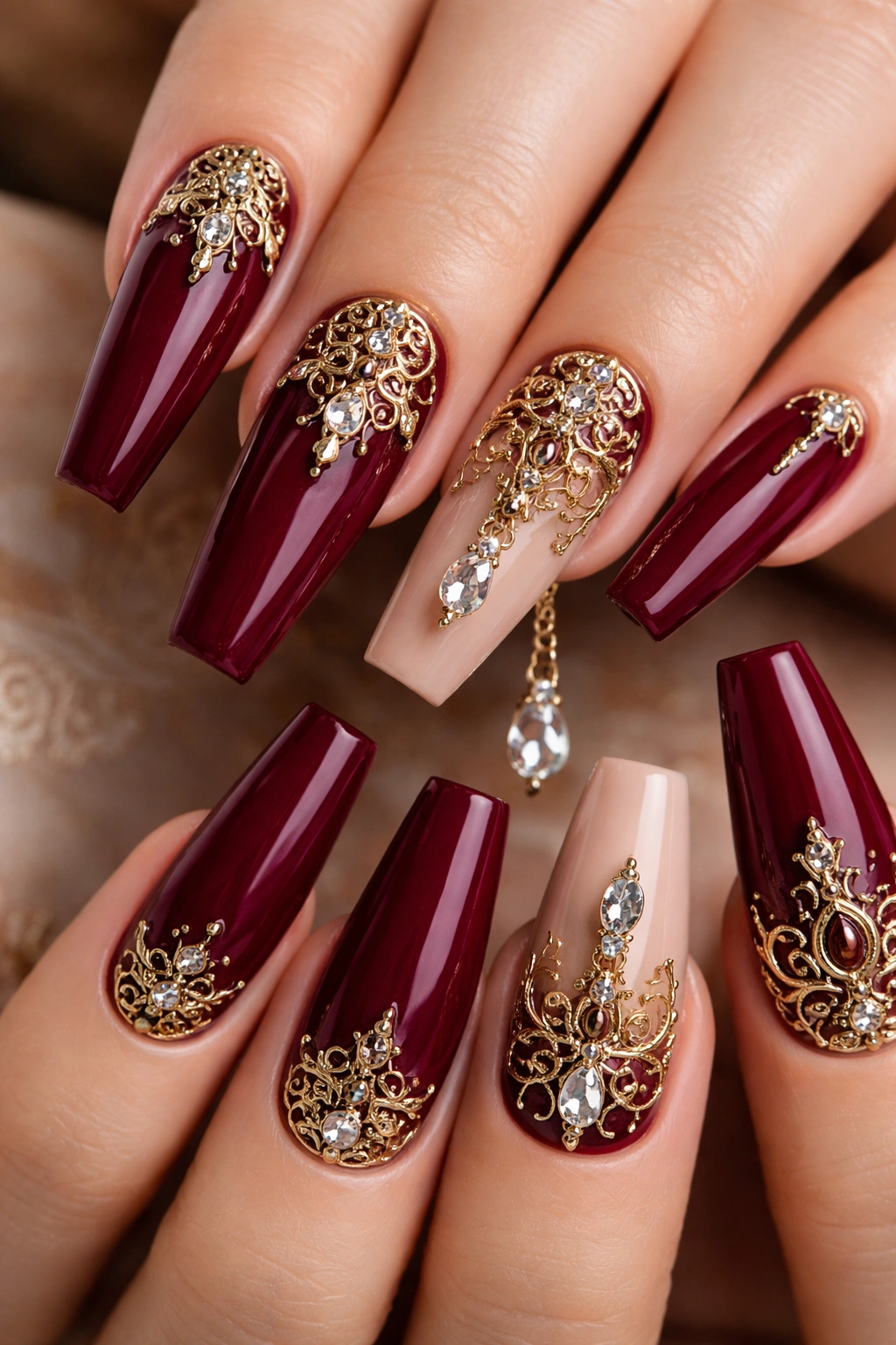 Close-up burgundy nails with ornate gold filigree charms