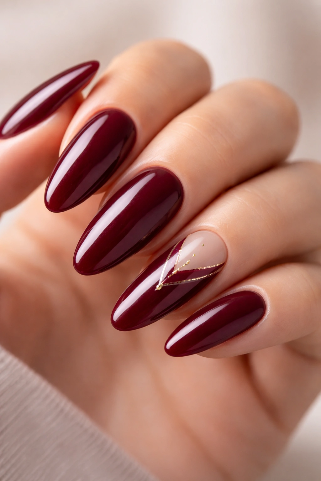 Close-up of burgundy long oval nails with subtle design accents on a neutral background