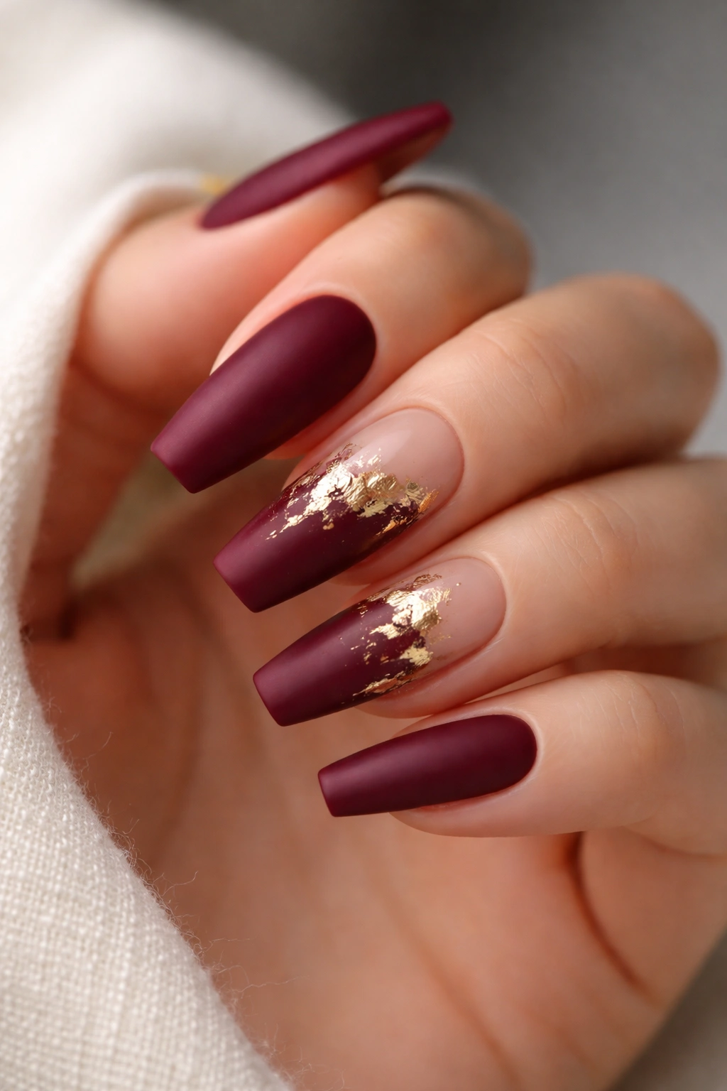 Close-up of medium coffin nails in deep burgundy with gold foil accents and negative space