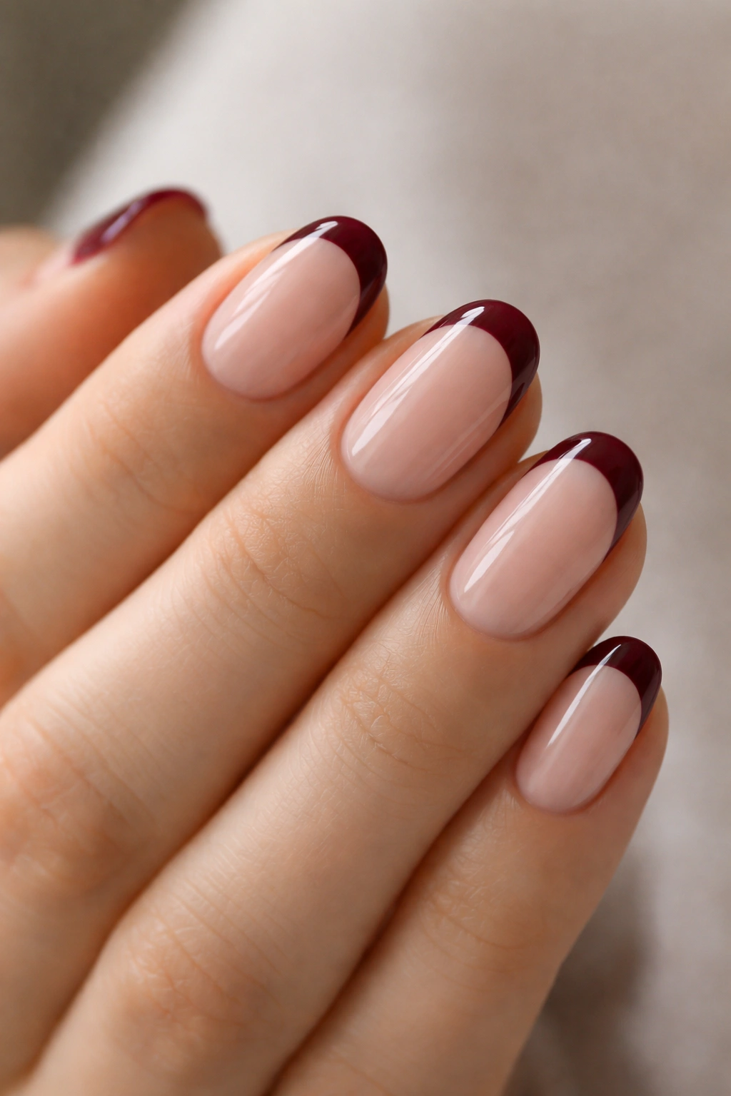 Close-up of short oval nails with nude base and burgundy French tips