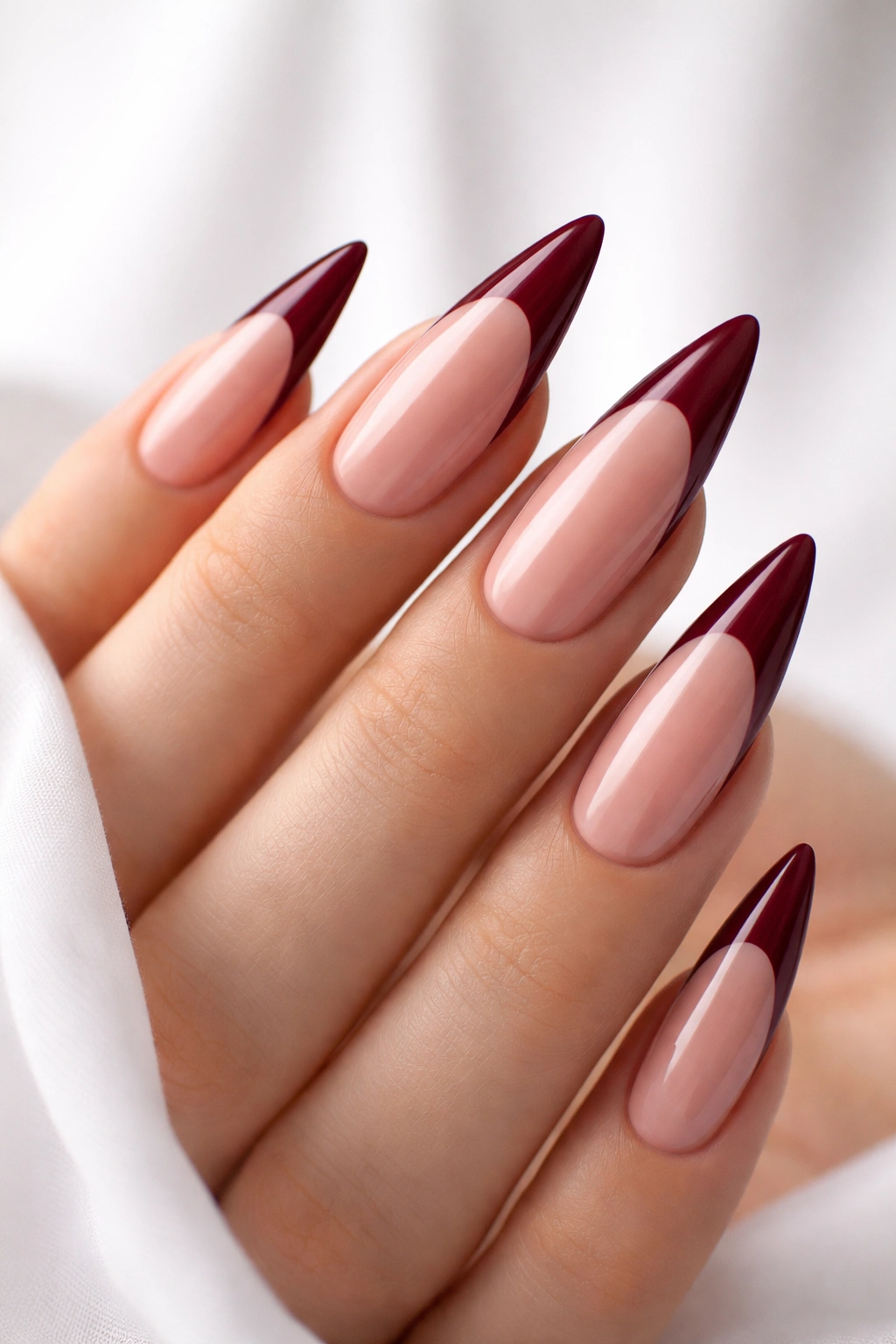 Close-up of long stiletto nails with nude base and glossy burgundy tips, studio lighting