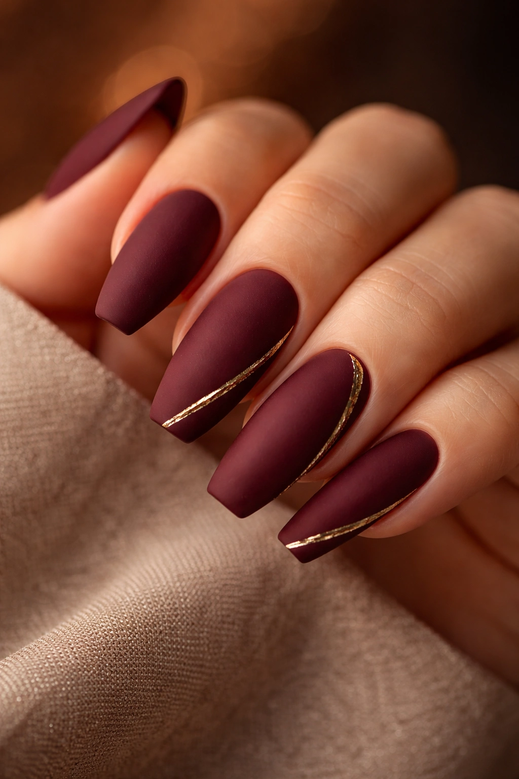 Matte burgundy acrylic nails with gold accents