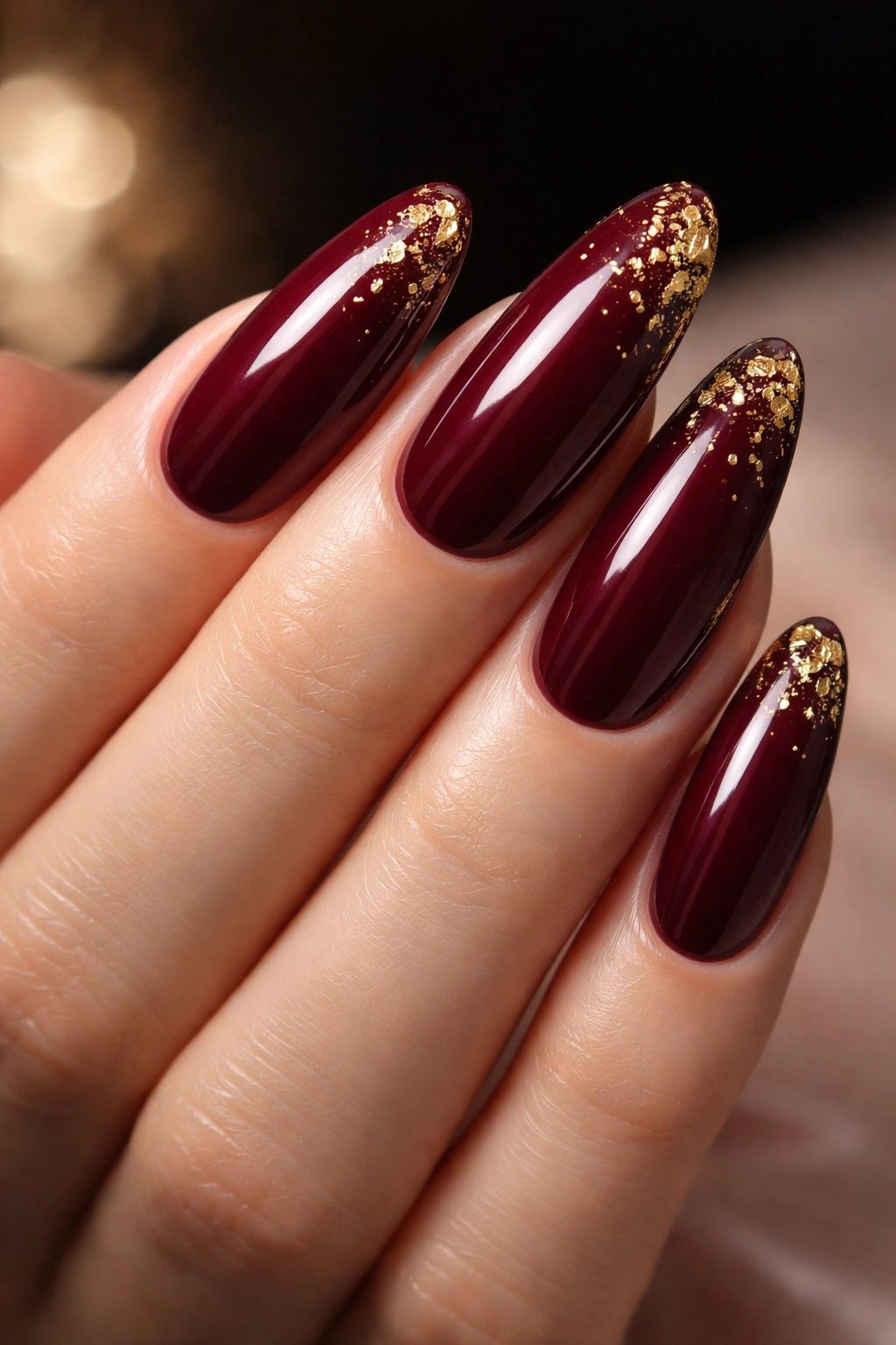 Close-up of deep burgundy nails with gold foil accents on long rounds