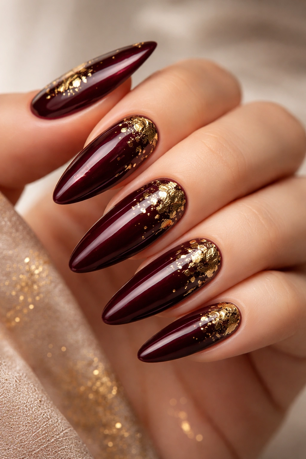 Close-up of burgundy nails with gold foil accents in an almond shape.