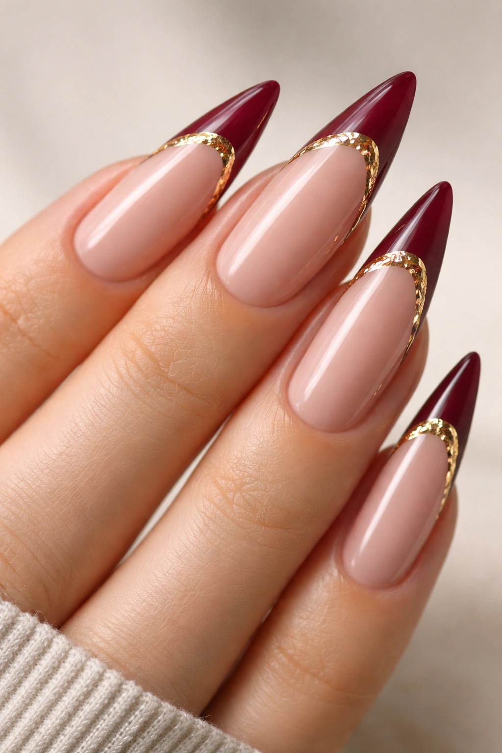 Close-up of burgundy French tips with gold foil accent on nude nails