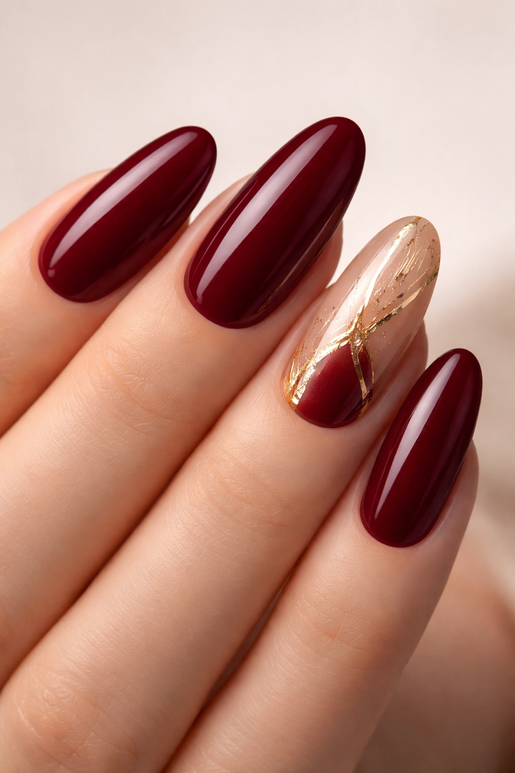 Nails with burgundy base and gold foil accents on ring fingers