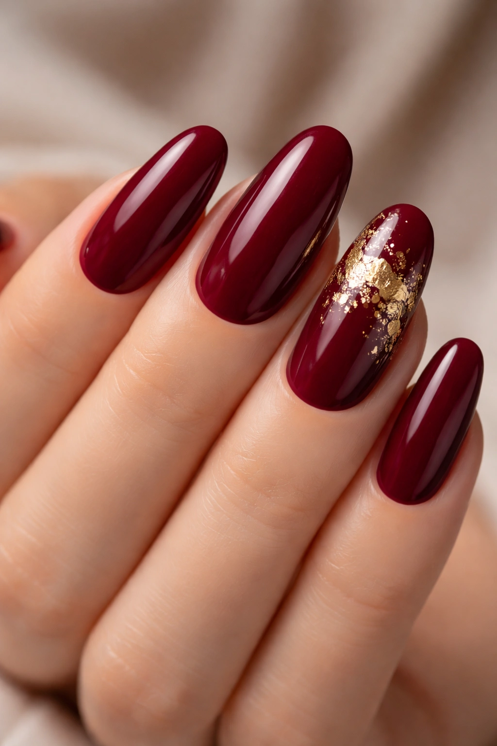 Close-up of burgundy nails with gold leaf accents on two nails.
