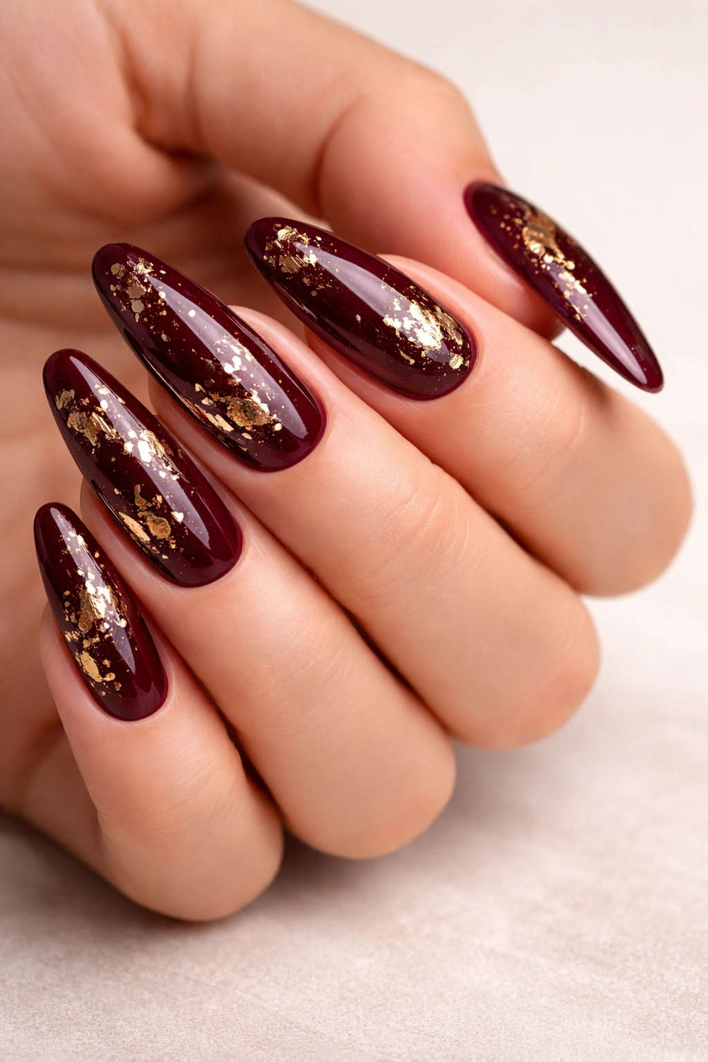Close-up of deep burgundy oval nails with gold leaf accents on a hand