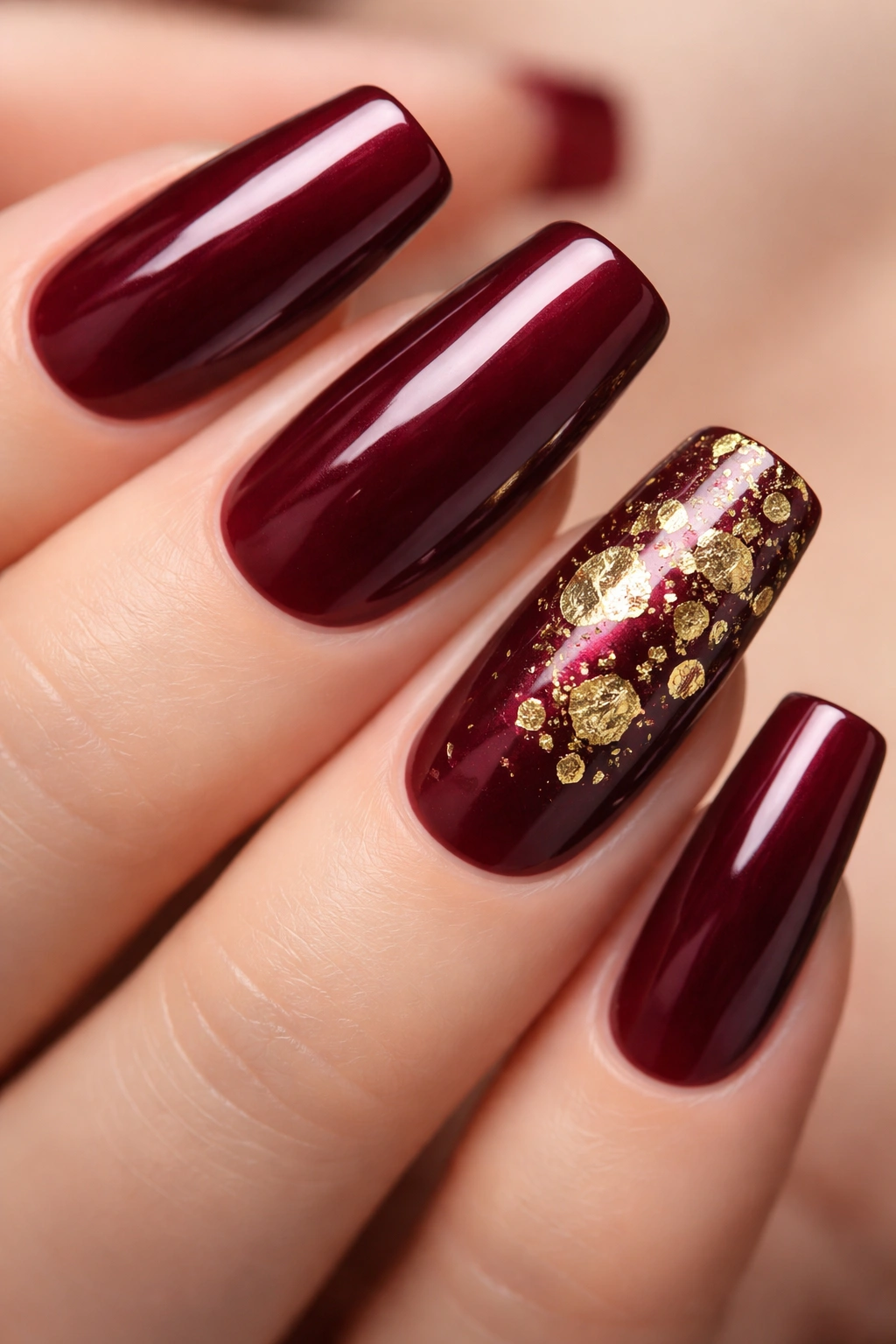 Close-up of long squoval nails in deep burgundy with gold leaf accents on one accent nail.