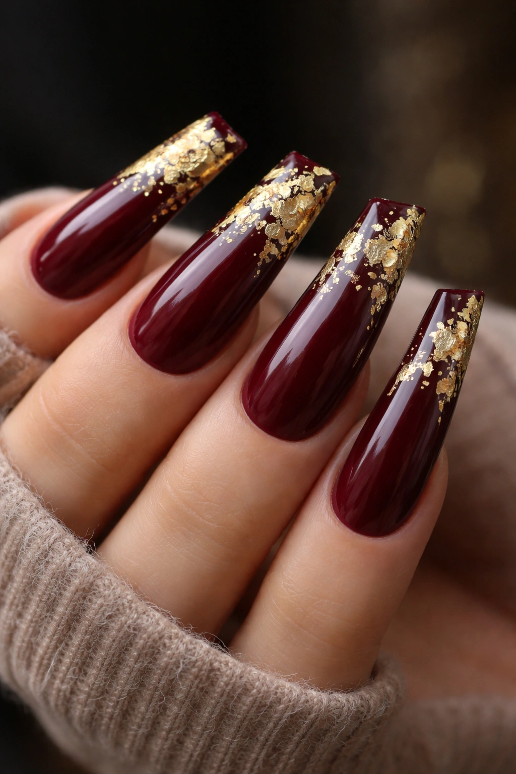Deep burgundy nails with gold leaf accents on long nails.