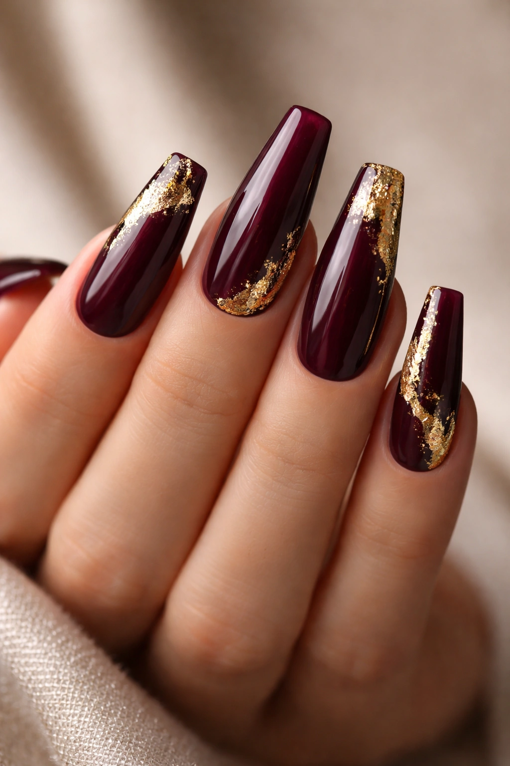 Close-up of burgundy coffin nails with gold leaf accents reflecting light