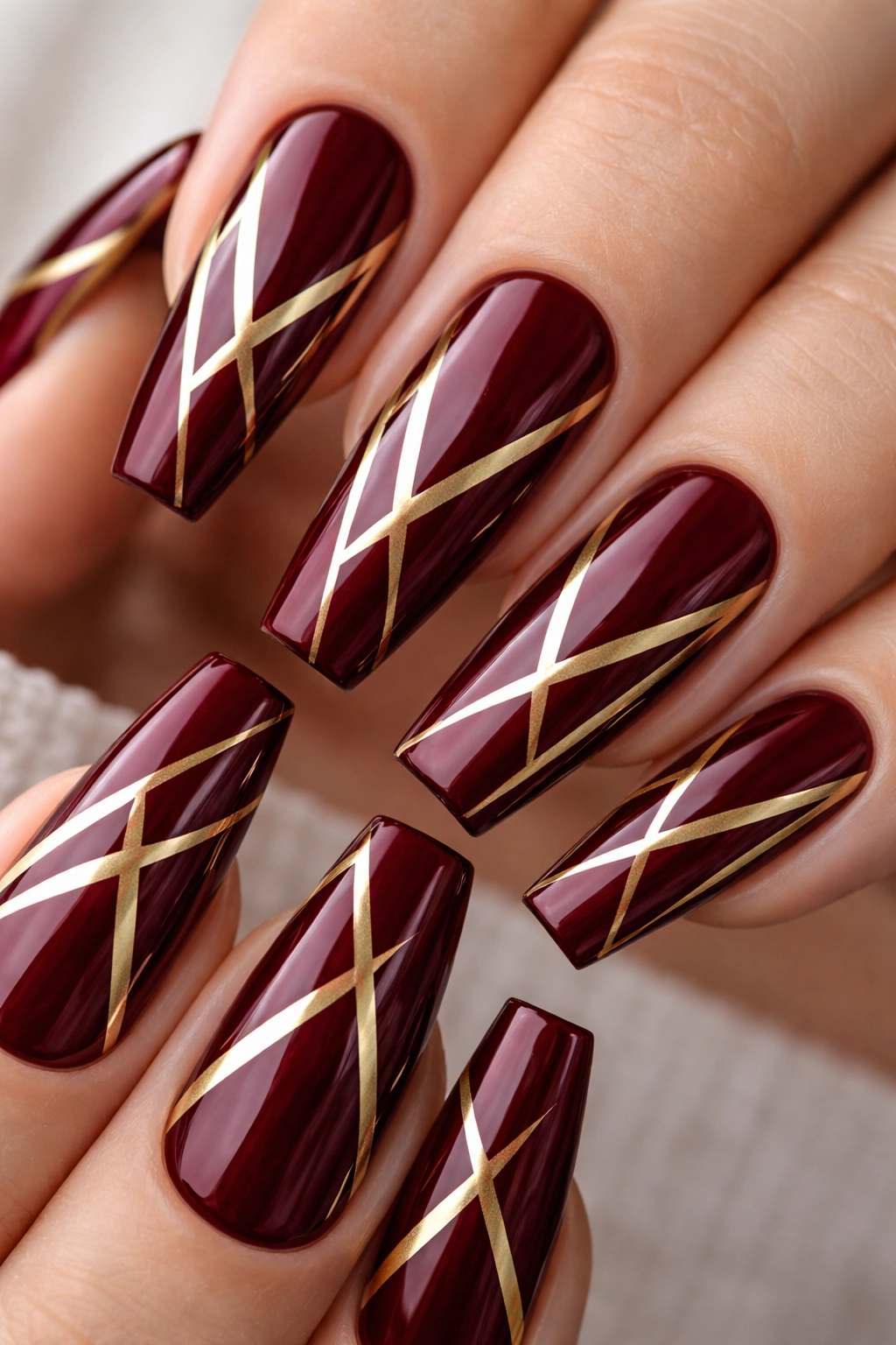 Close-up of burgundy coffin nails with gold geometric triangles.
