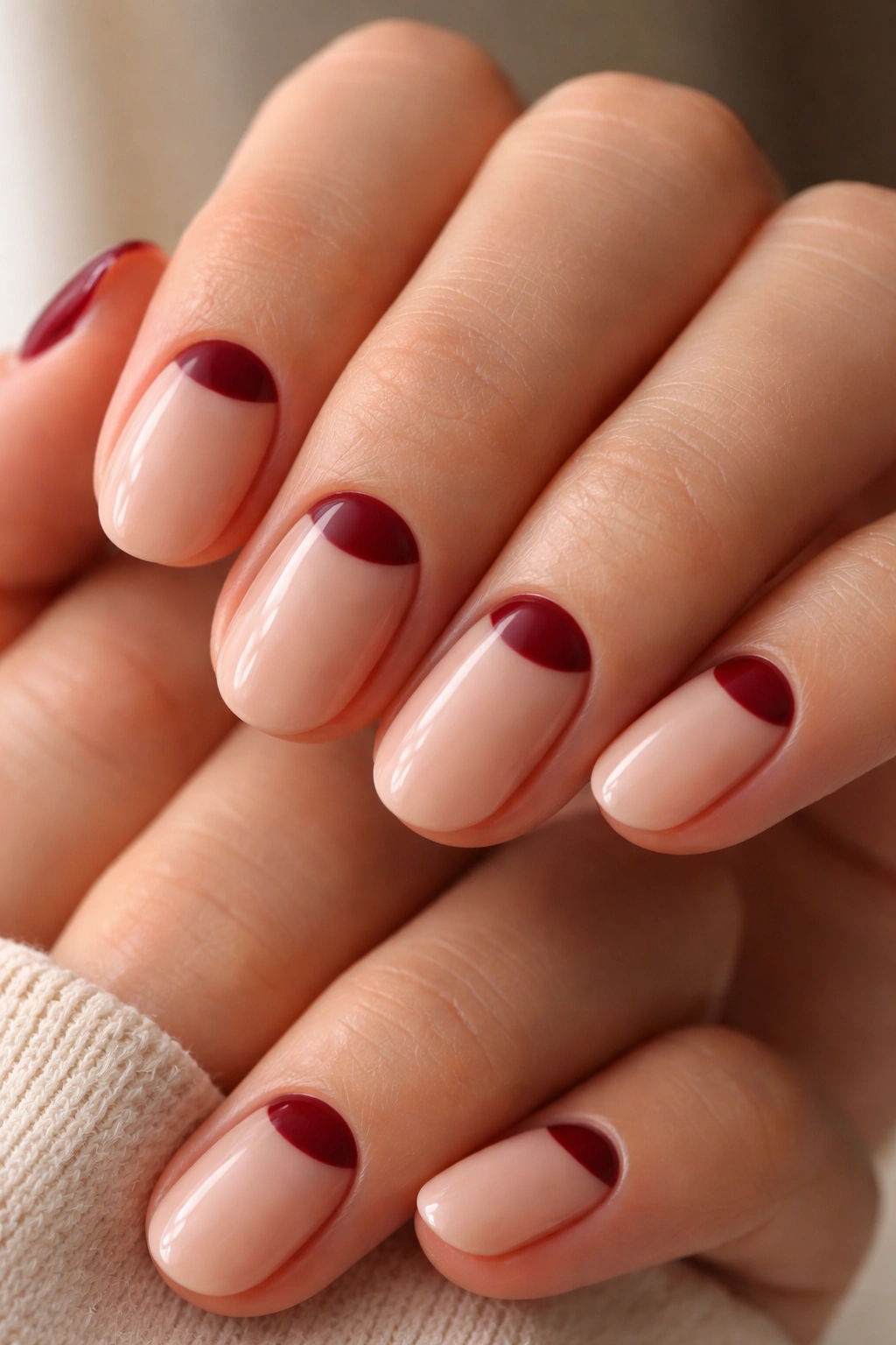 Burgundy half-moon nails on short oval nails on a nude base.