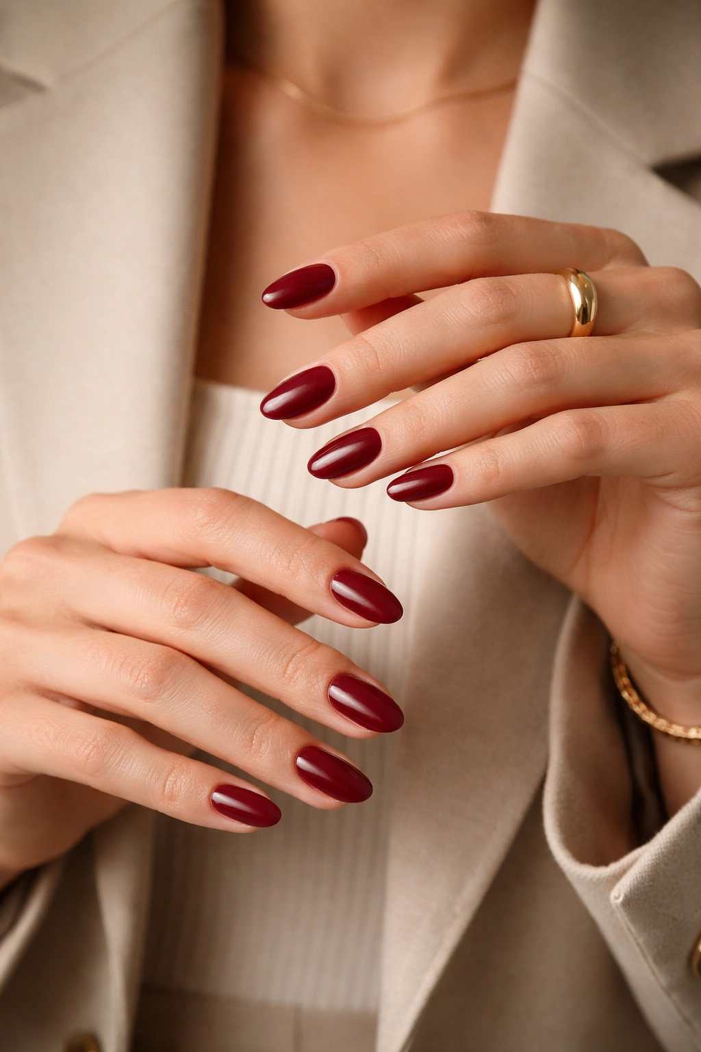 Close-up of burgundy short almond nails with gold ring and bracelet