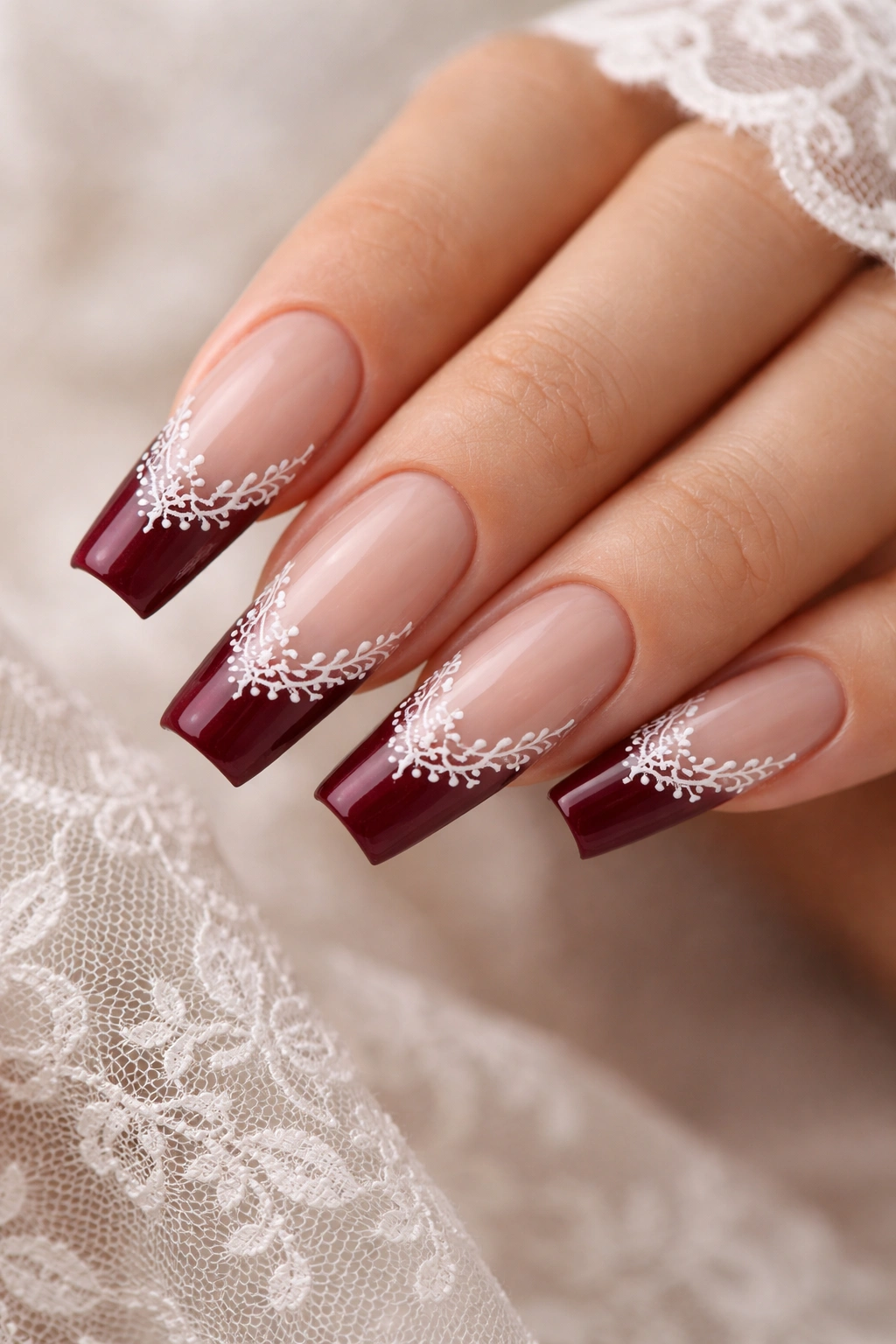 Close-up of burgundy-tipped coffin nails with white lace detailing.