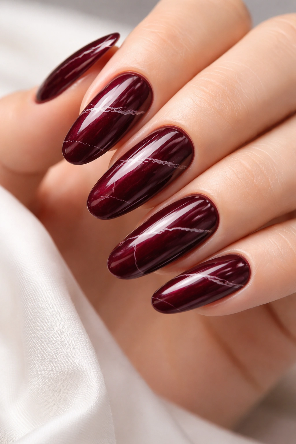 Deep burgundy long round nails with subtle white marble veining