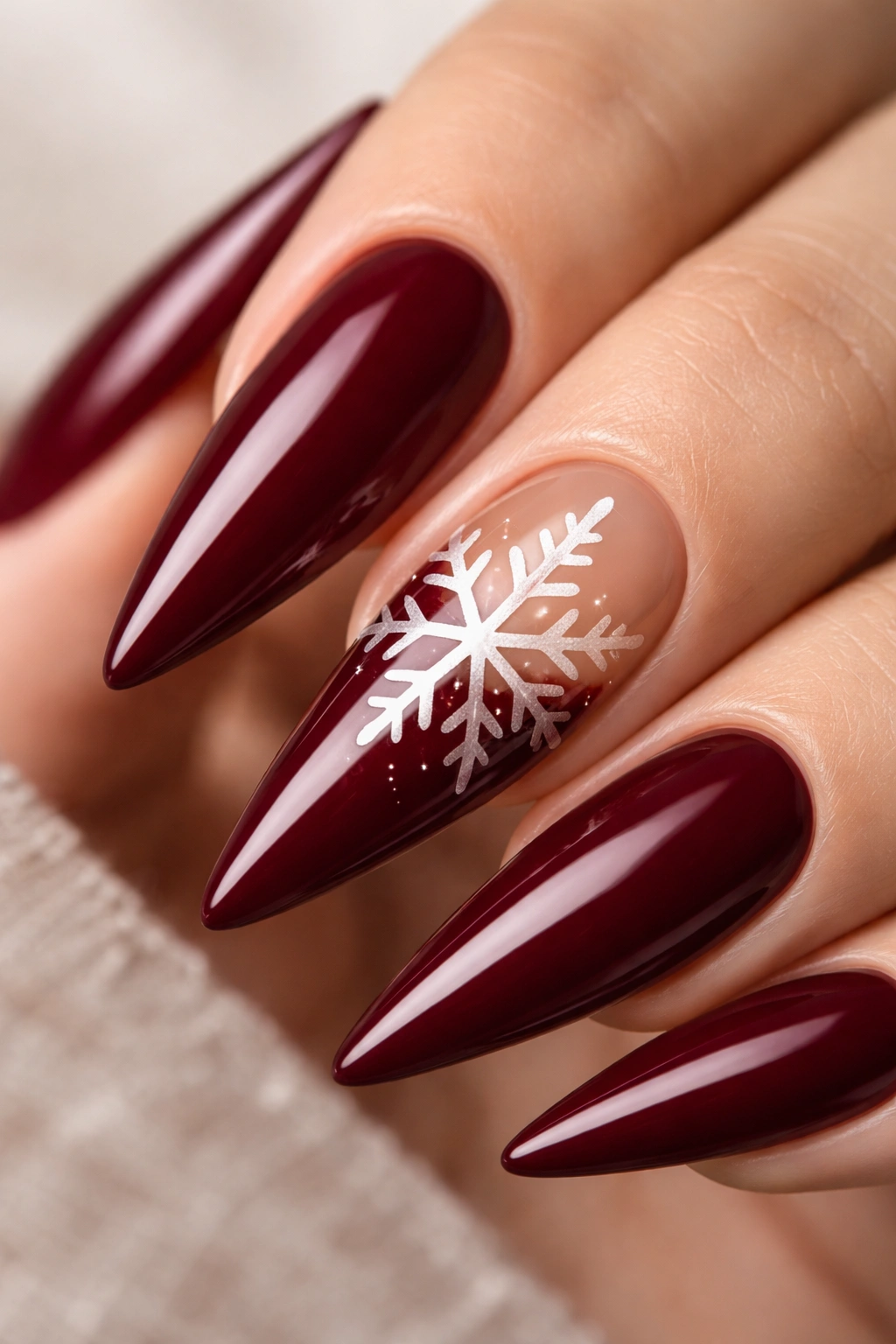 Close-up of burgundy stiletto nail with negative-space snowflake silhouette on a neutral background