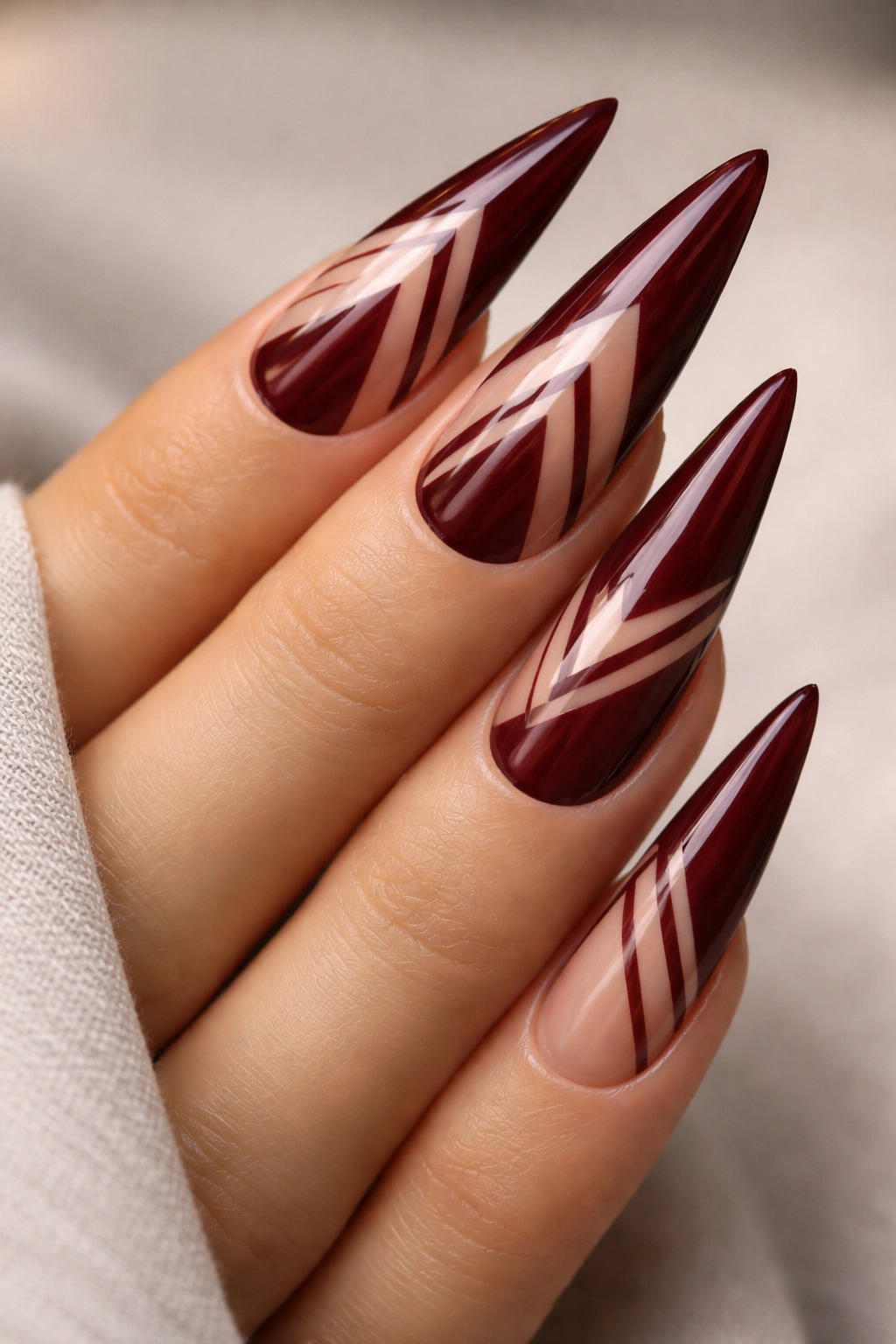 Burgundy stiletto nails with negative space geometric patterns.