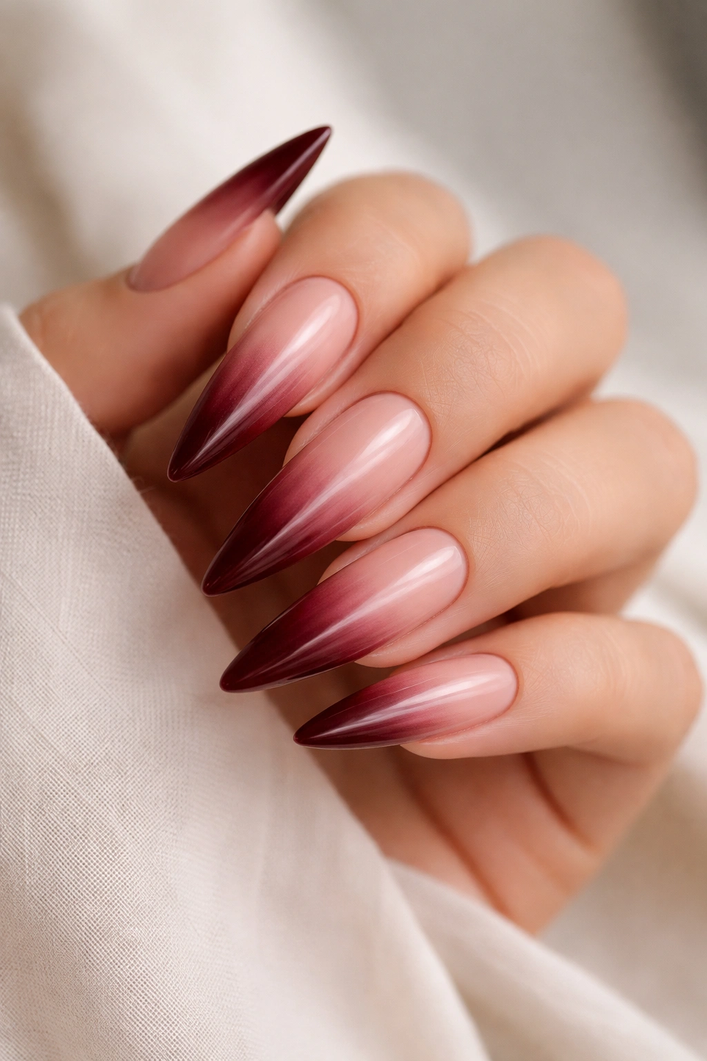 Close-up of sheer burgundy ombre stiletto nails on nude base