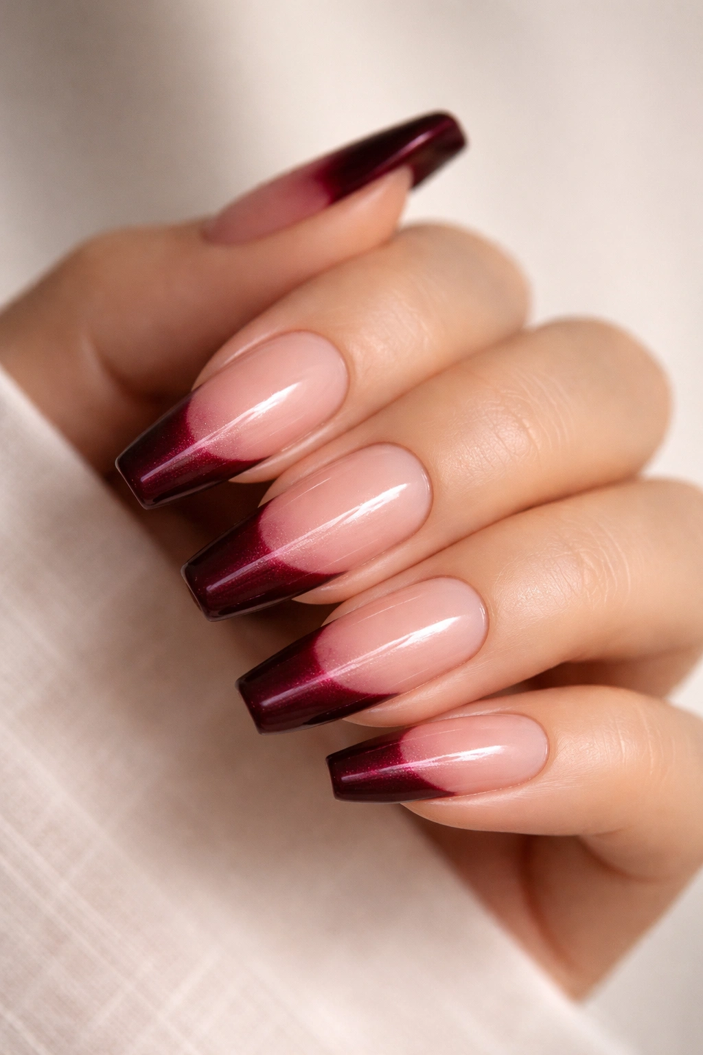 Close-up of nails with burgundy tips featuring subtle pearl shimmer.