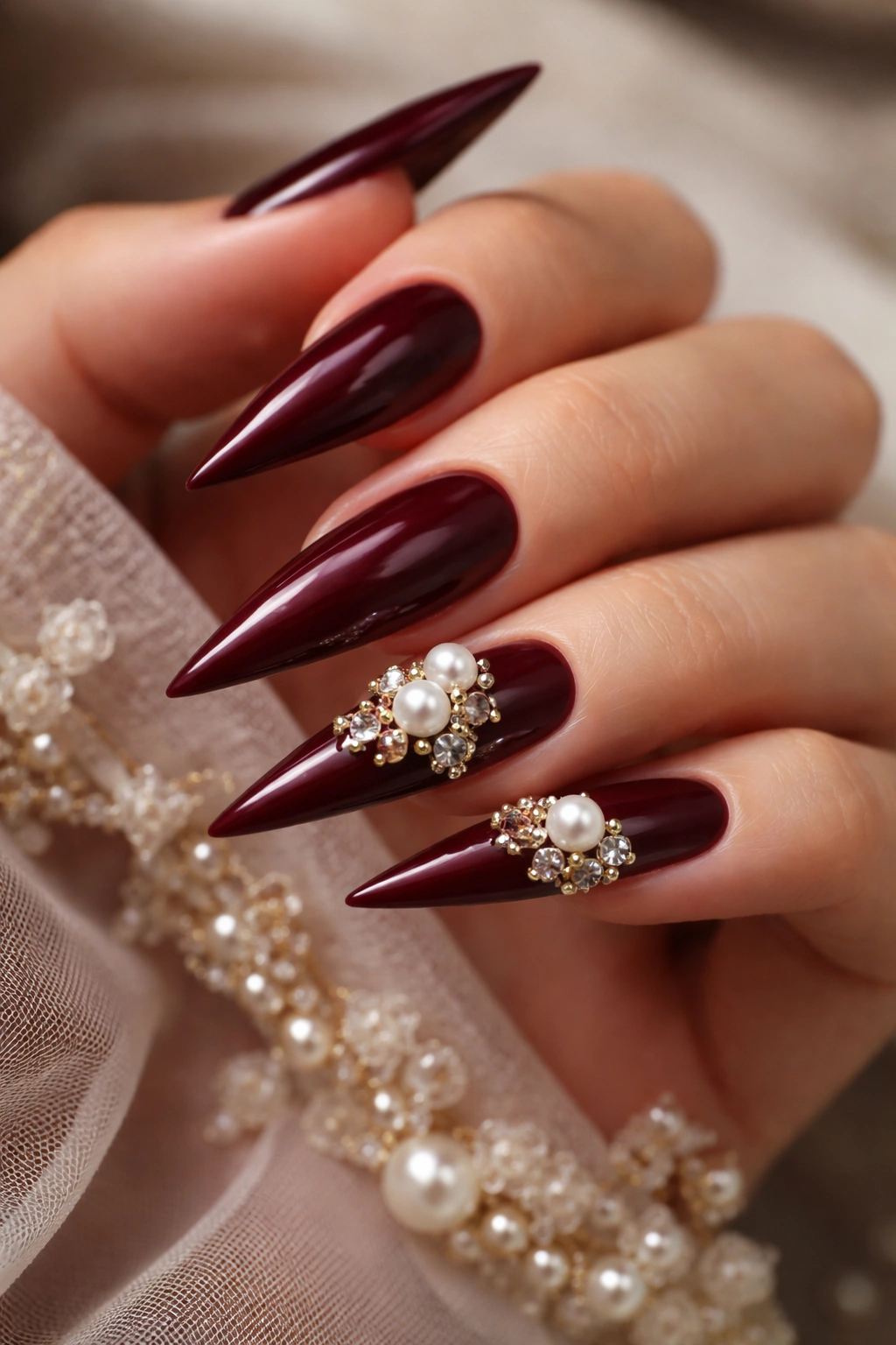 Close-up of deep burgundy nails with pearl charms at tips