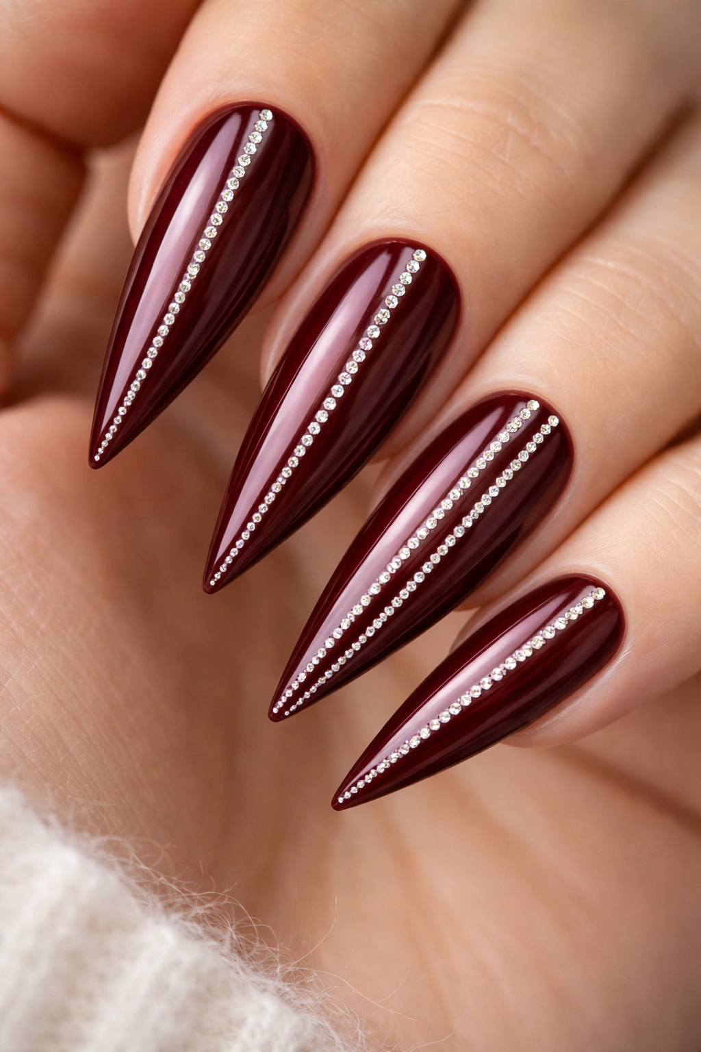 Close-up of wine-toned burgundy nails with rhinestone pinstripes