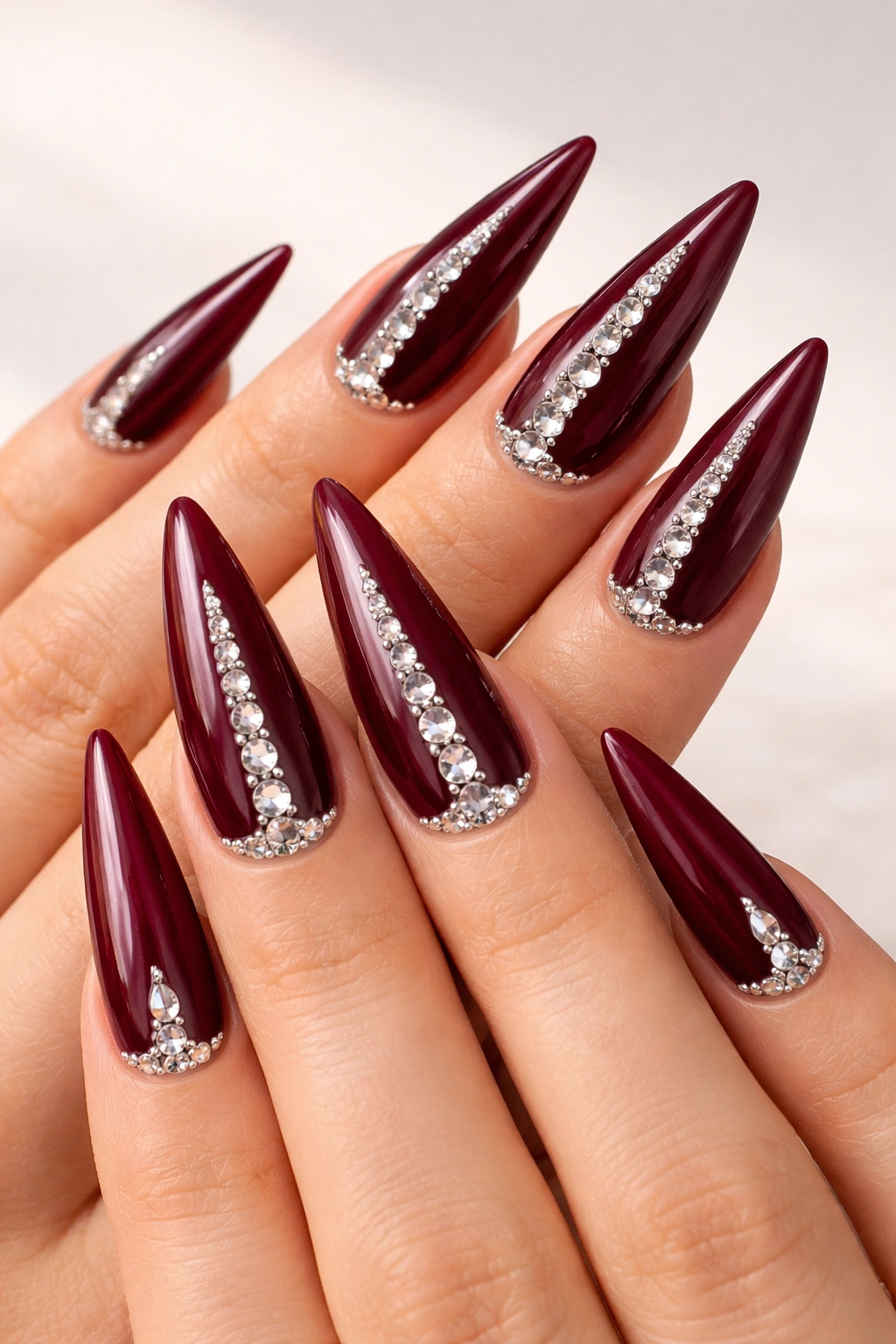 Close-up of burgundy stiletto nails with rhinestones along the cuticle and center