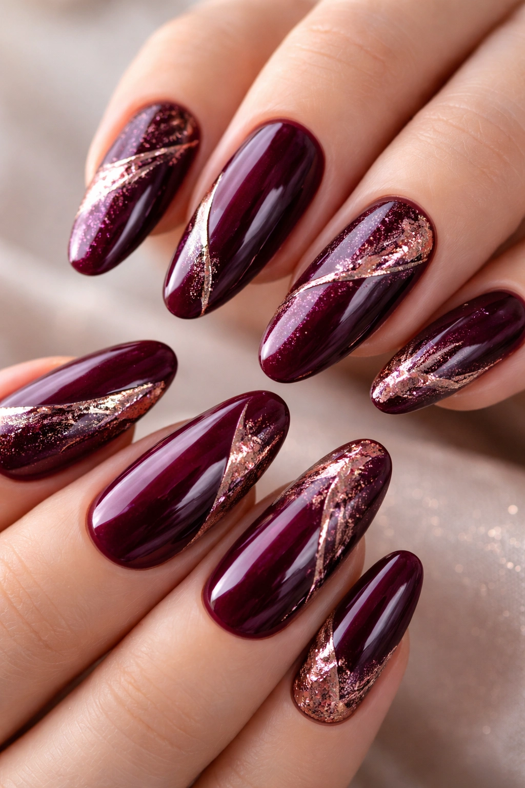 Close-up of deep burgundy purple nails with rose-gold foil accents and glossy finish.