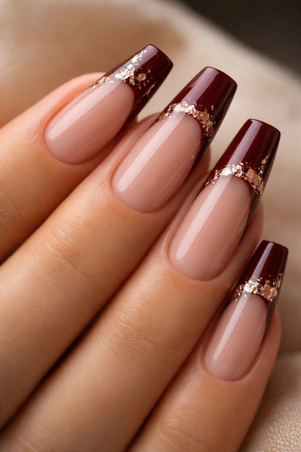 Close-up of dark burgundy nails with rose gold foil accents on the tips.