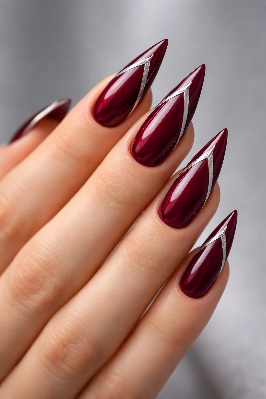 Close-up of burgundy stiletto nails with metallic accents along sides and tip.