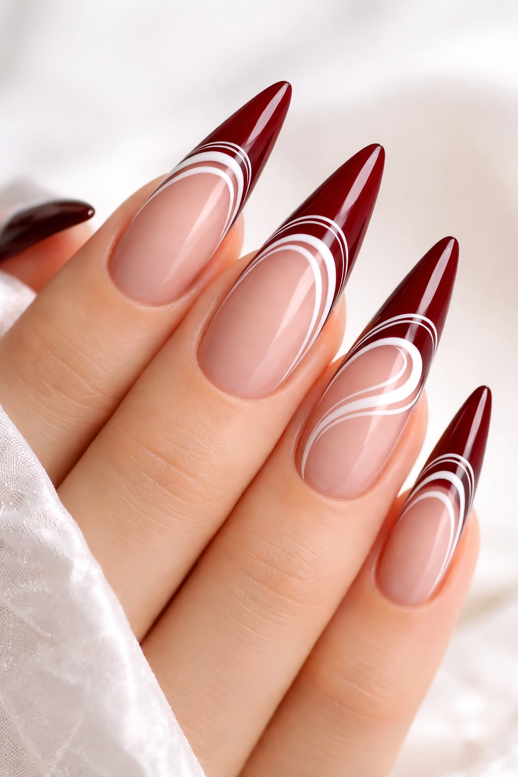 Close-up of burgundy nails with white swirl details on nude base