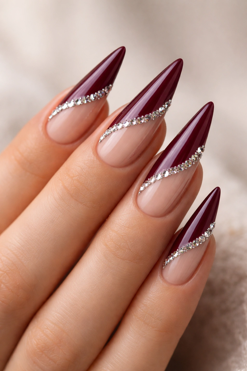 Burgundy nails featuring negative space and rhinestones with a clean minimalist backdrop