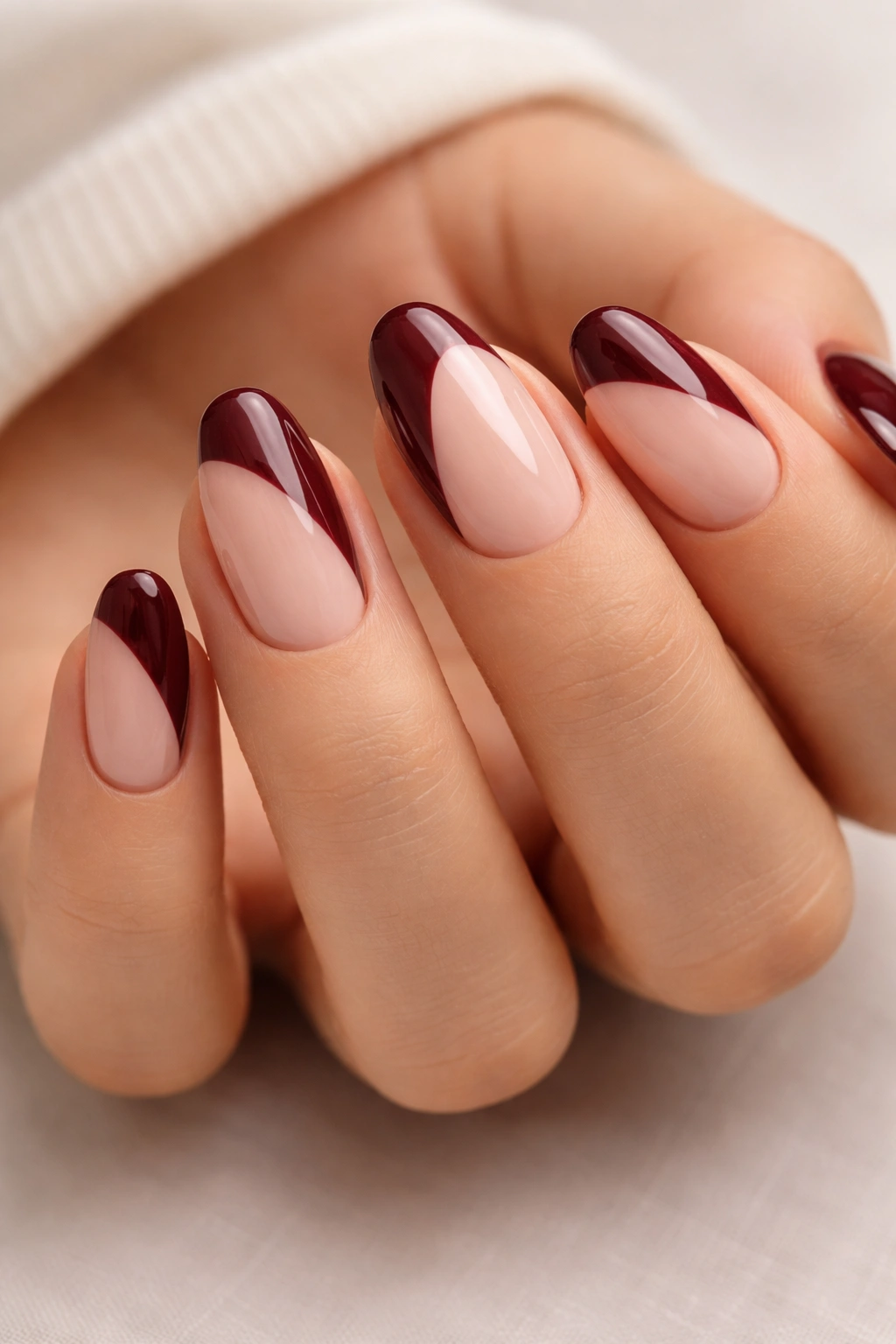 Close-up of short almond nails with nude base and burgundy tips showing contrast.