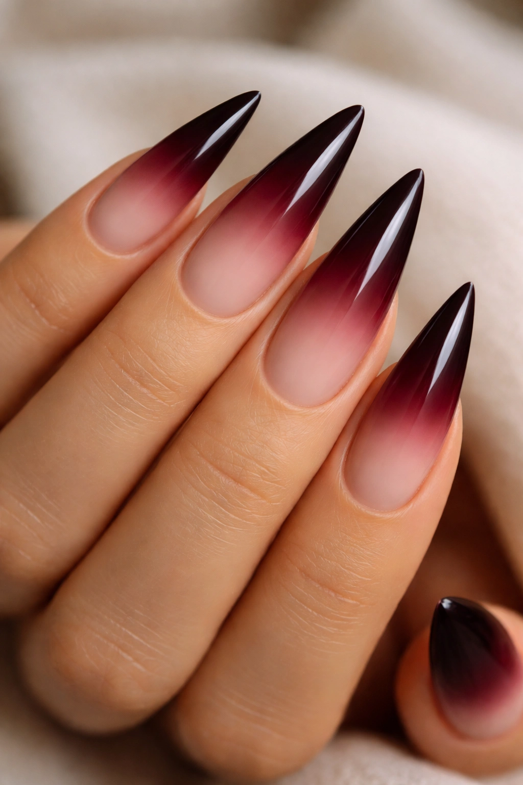 Close-up of burgundy to nude ombre stiletto nails on a hand