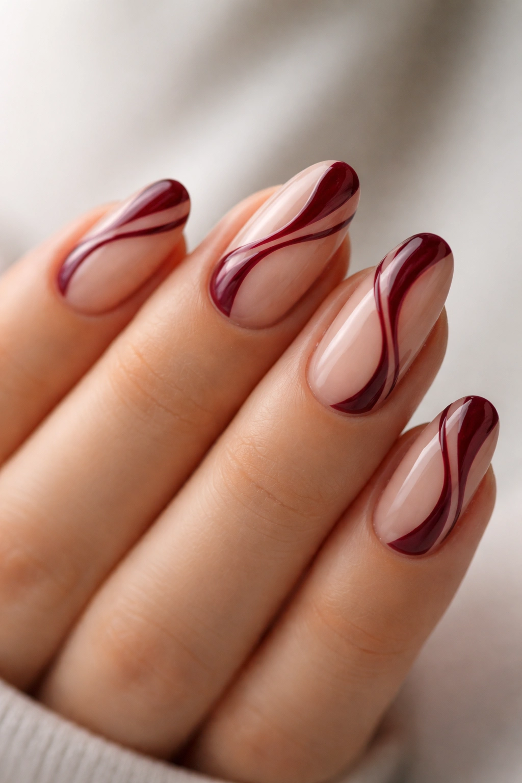 Close-up of burgundy and nude swirl manicure on short almond nails.